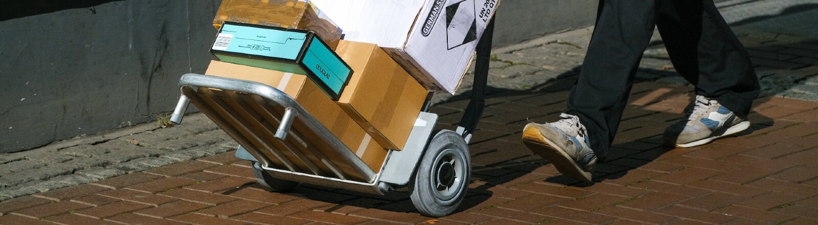 Ein Paketbote schiebt eine mit Paketen voll beladene Sackkarre.