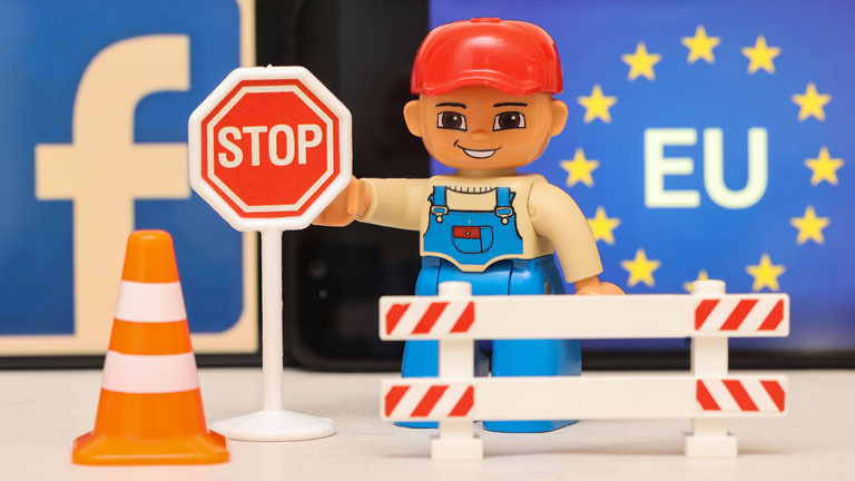 Kinderspielzeug: Bauarbeiter mit Stoppschild und Zaun vor Facebook und EU-Logo