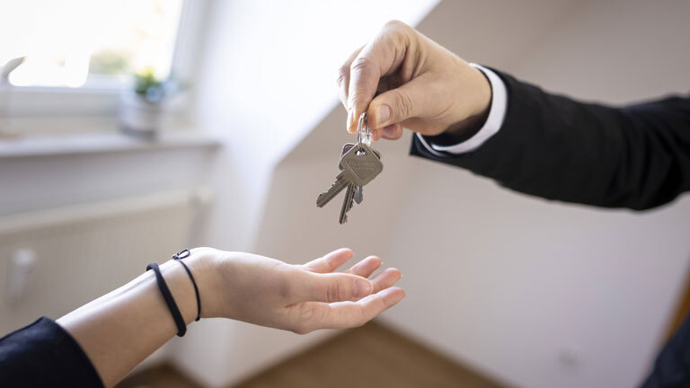 Ein Makler oder Vermieter übergibt einen Schlüssel an einen neuen Vermieter.