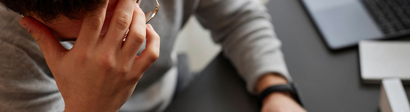 Ein Mann sitzt vor einer Tastatur und hält nachdenklich die eine Hand an seiner Stirn.
