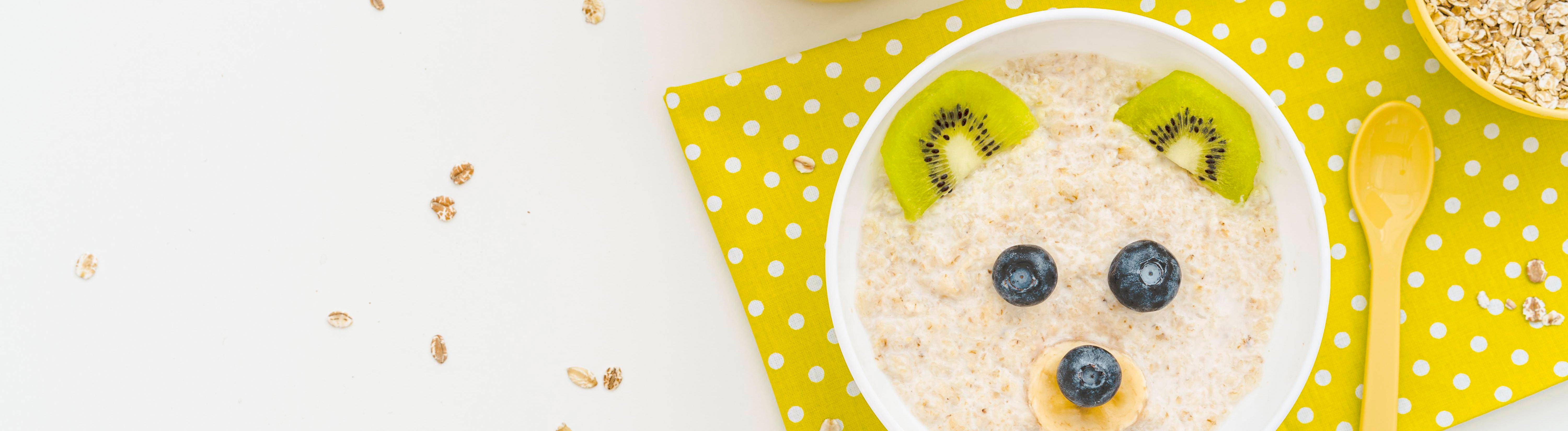 Eine Schale mit Porridge und Beeren, daneben Haferflocken und Bananen.