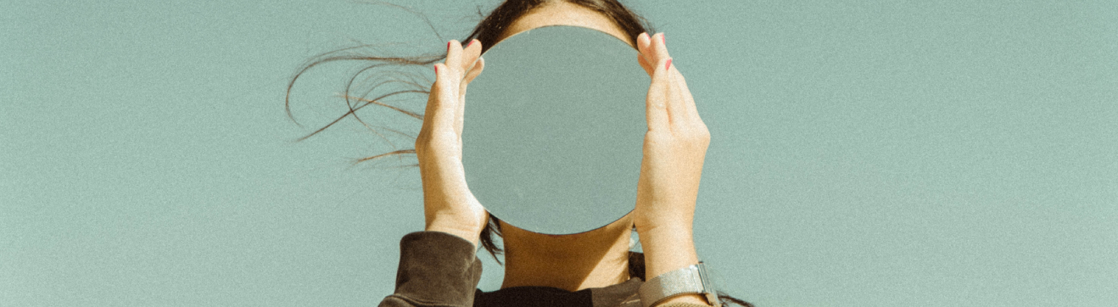 An abstract image of a female holding a mirror in front of her face with the color of the sky