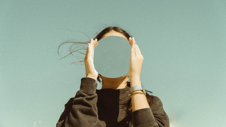 An abstract image of a female holding a mirror in front of her face with the color of the sky