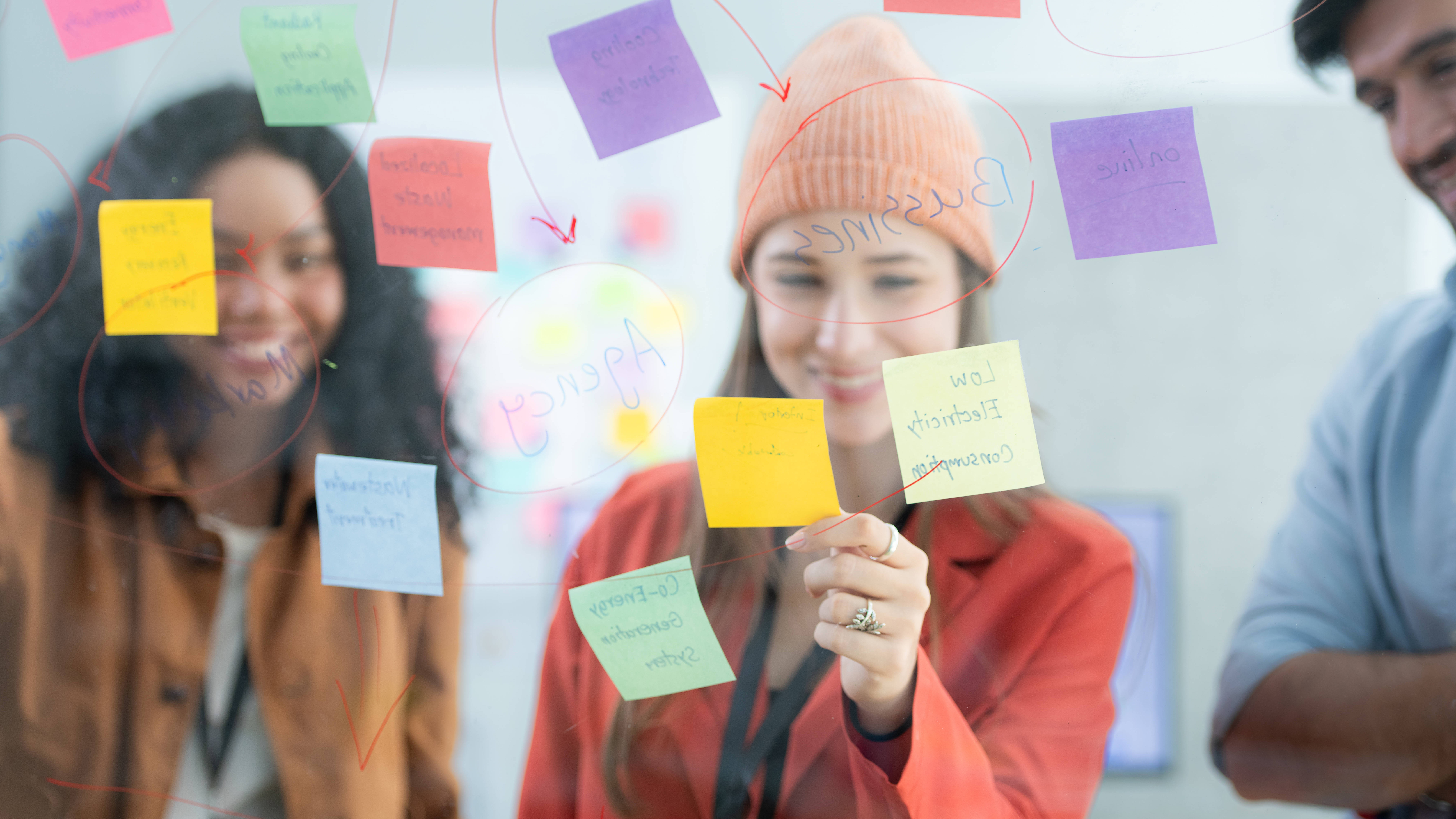 Drei junge Menschen stehen vor einer Wand mit Post-its und Notizen.