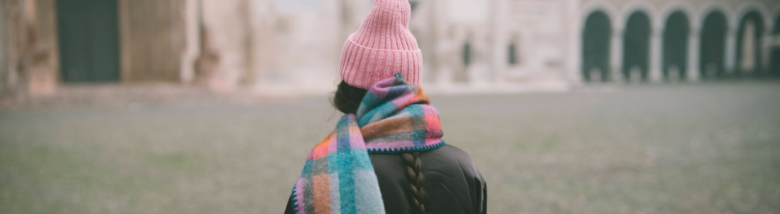 Eine Frau mit pinker Mütze und einem bunten Schal wendet sich von der Kamera ab.