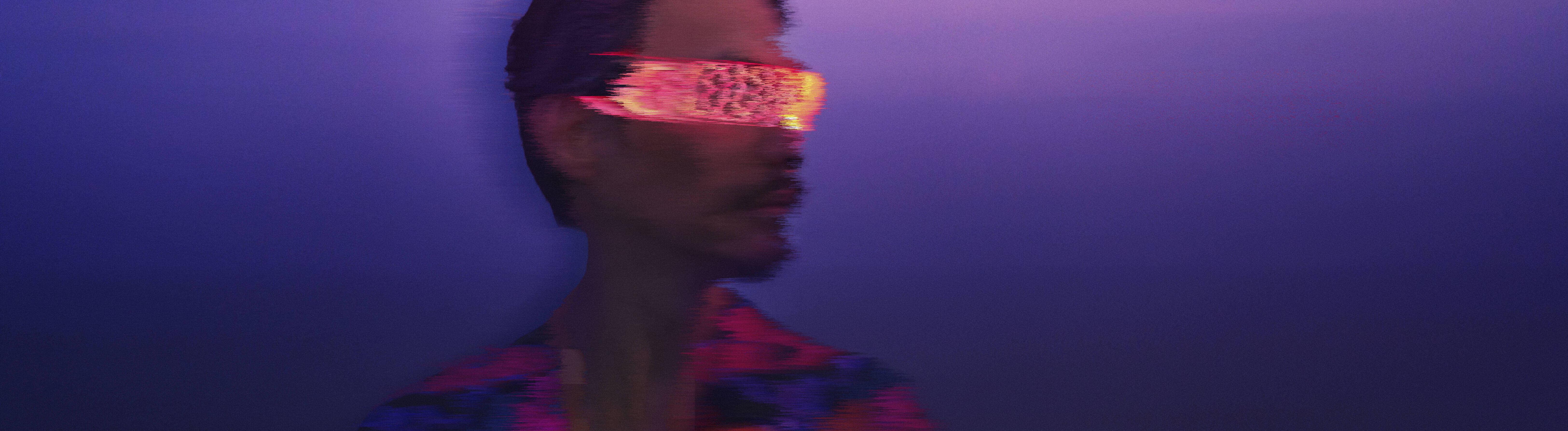 Ein Mann trägt eine pink-orange leuchtende schmale VR-Brille. Er befindet sich draußen. Es scheint, als gehe es von der Dämmerung in die Nacht über. Das Bild ist leicht verschwommen.