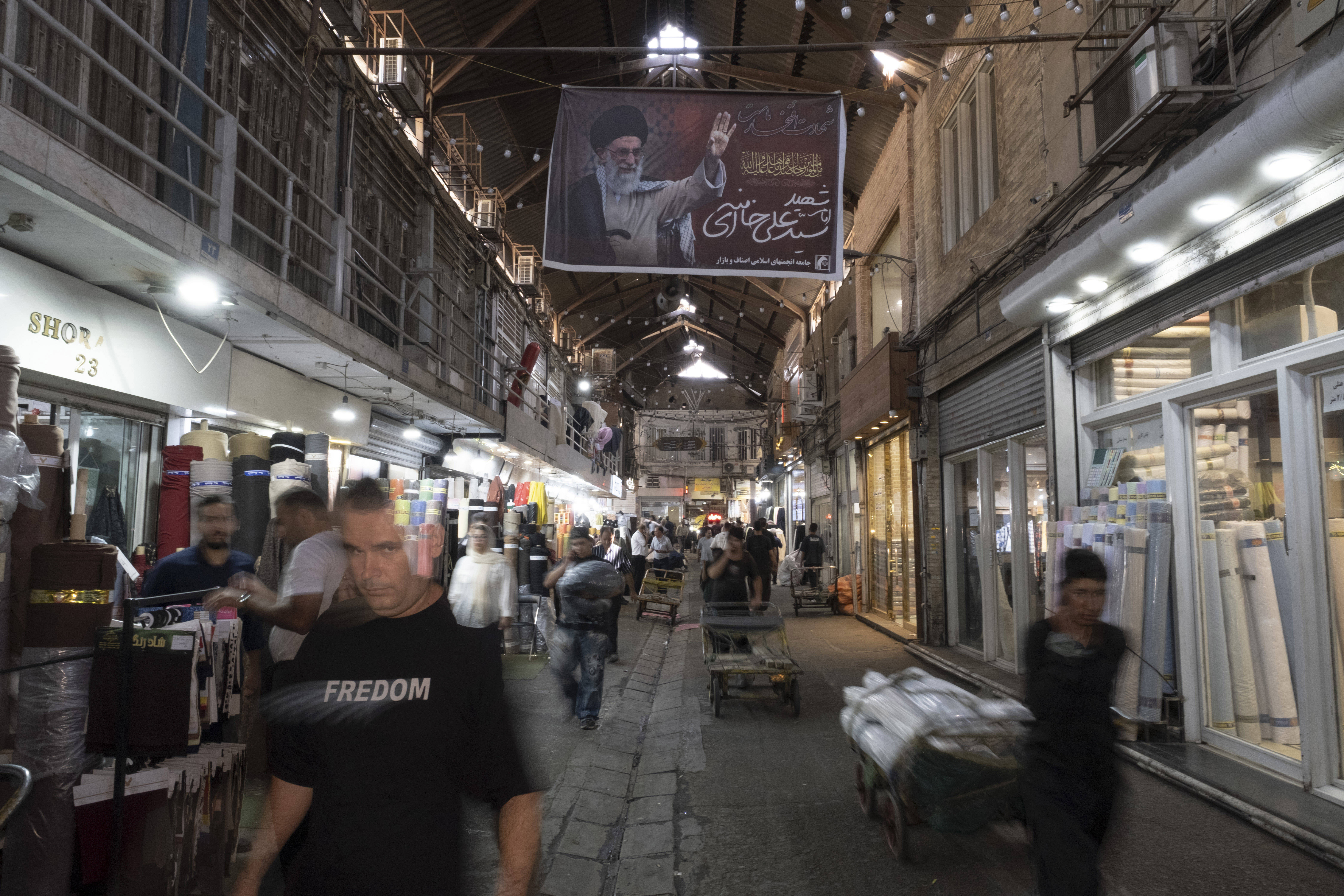 Iranische Lastträger transportieren Waren mit Karren unter einem Porträt des verstorbenen obersten Führers des Iran, Ayatollah Ali Khamenei, durch den traditionellen Großen Basar im Süden von Teheran, Iran. 1.9.2026
