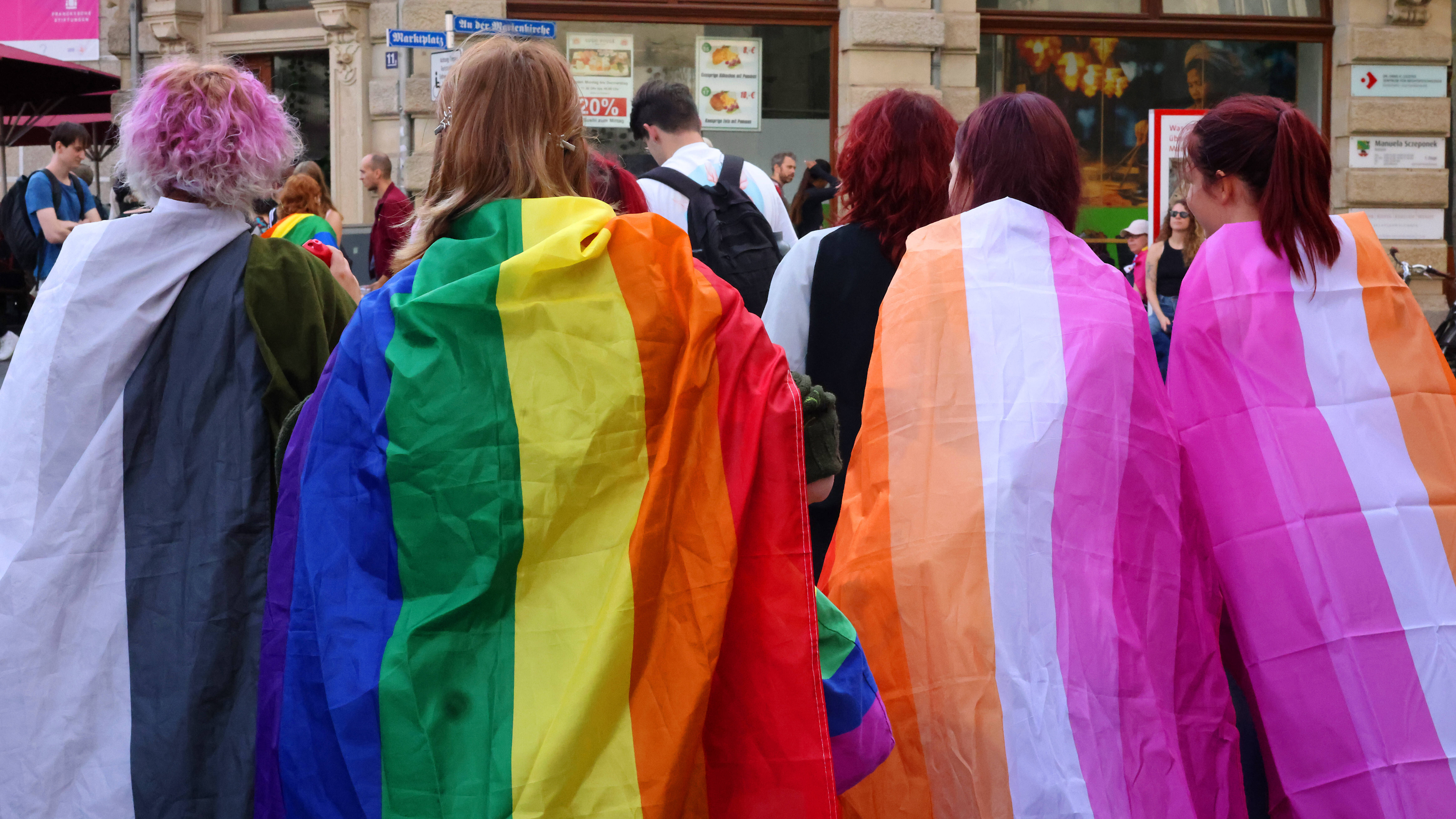 Vier Teilnehmende der CSD-Demonstration von hinten in bunte Flaggen gehüllt (Halle, 12.09.2026)