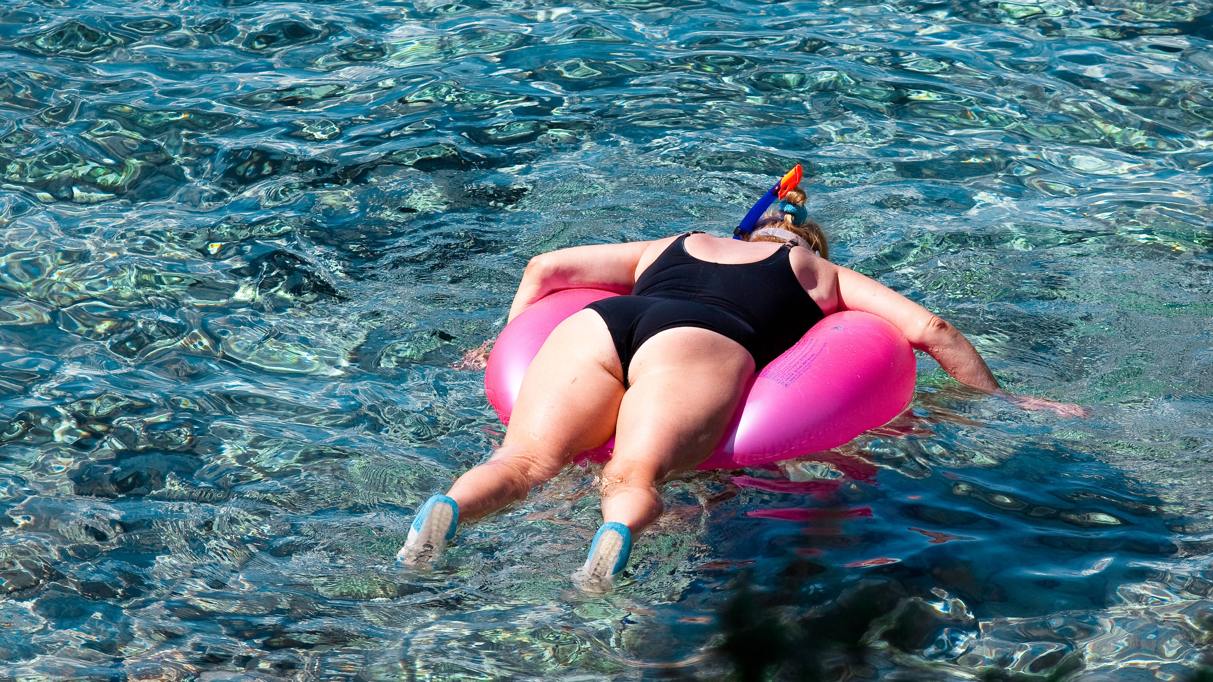 Eine Frau im schwarzen Badeanzug liegt auf einem pinken Schwimmreifen und schnorchelt.