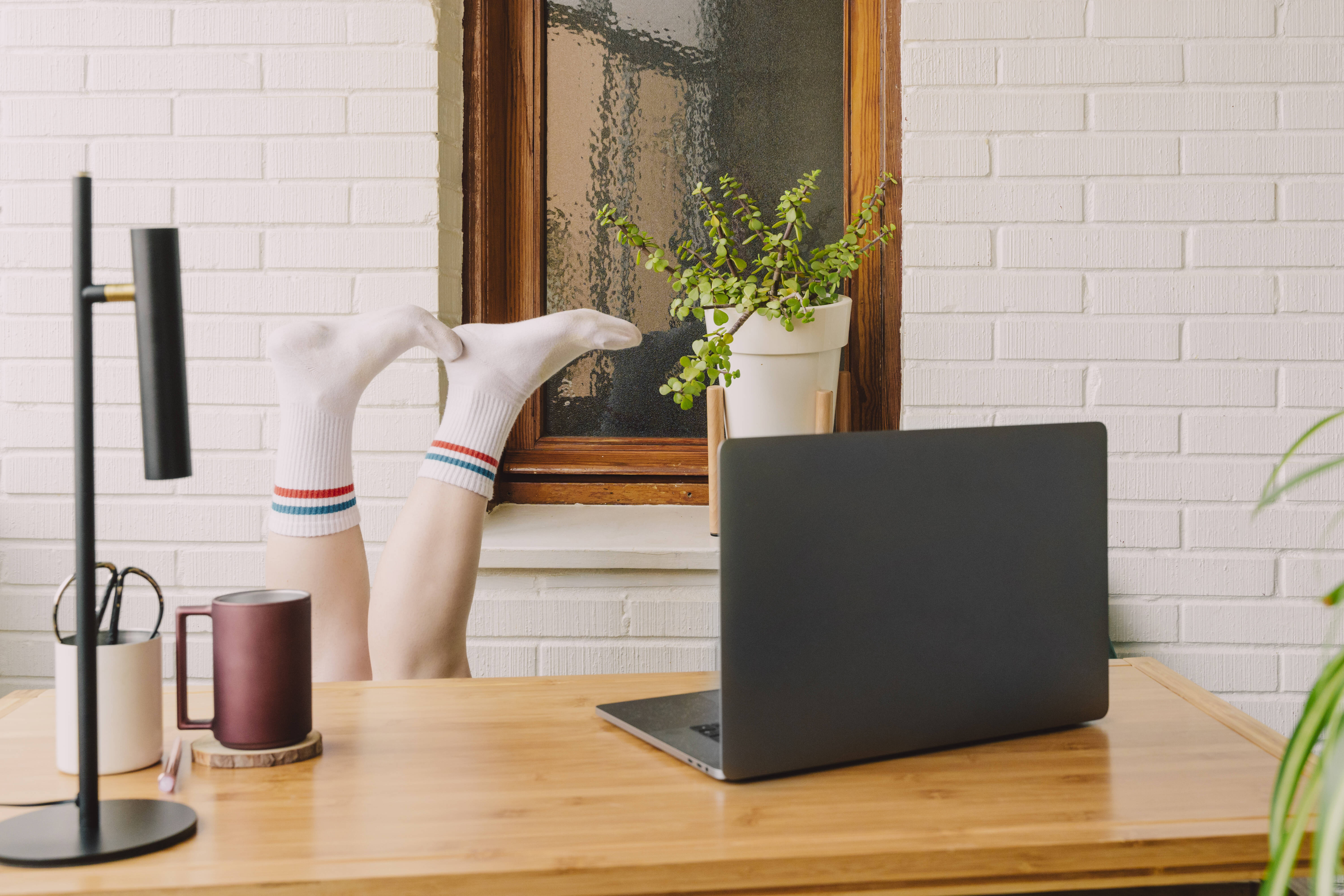 Gelangweilte Frau mit hochgelegten Füßen am Laptop am Tisch im Homeoffice.