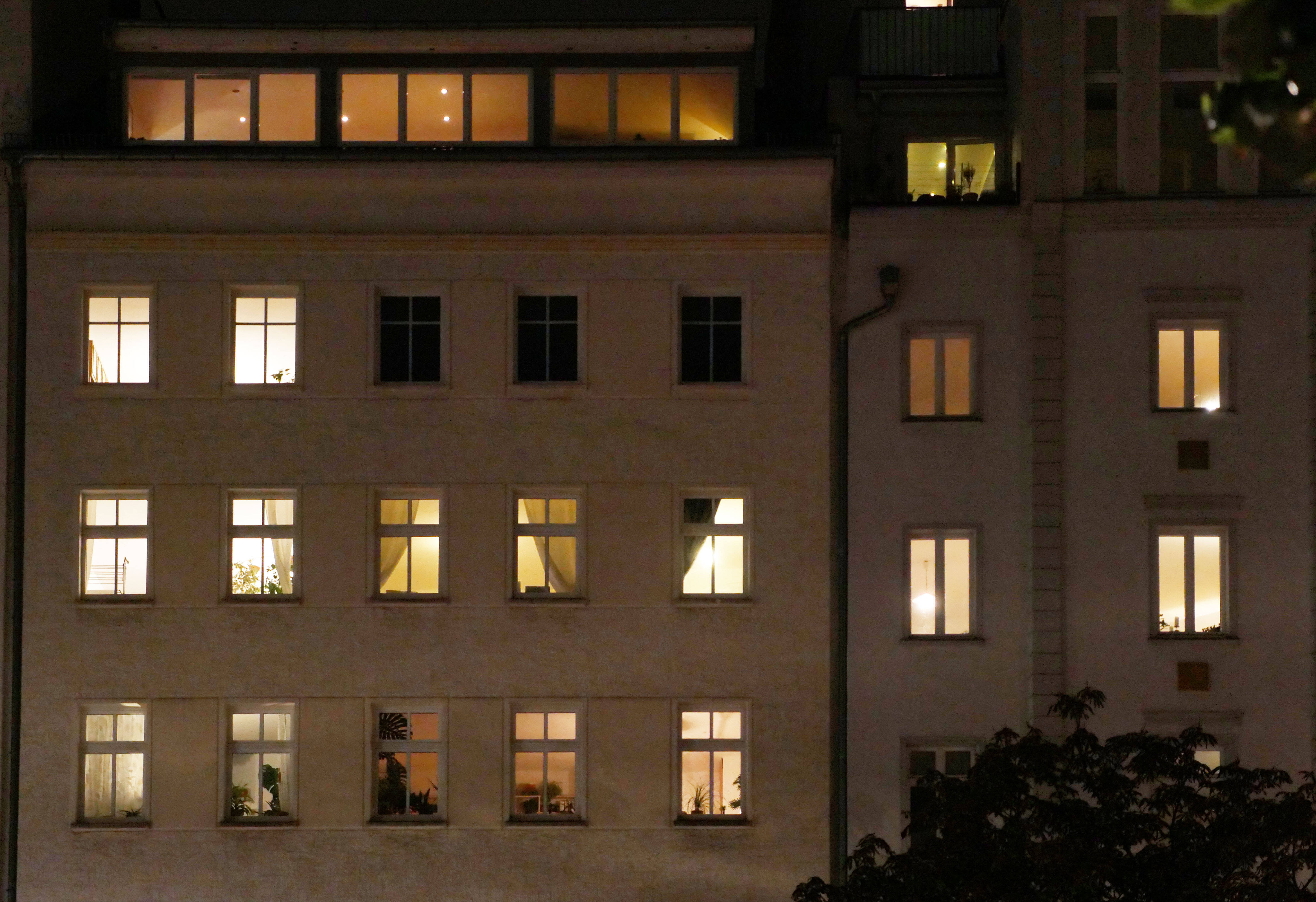 Ein Mehrfamilienhaus am Abend. Die meisten Fenster sind erleuchtet.