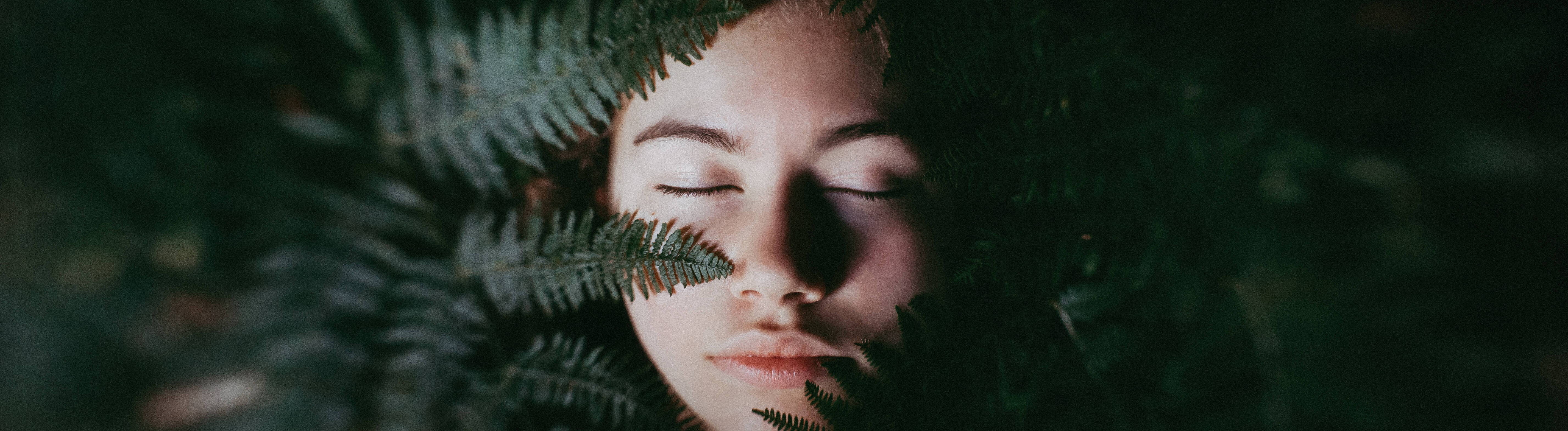 Das Gesicht eines jungen Menschen im Vordergrund ein Farn