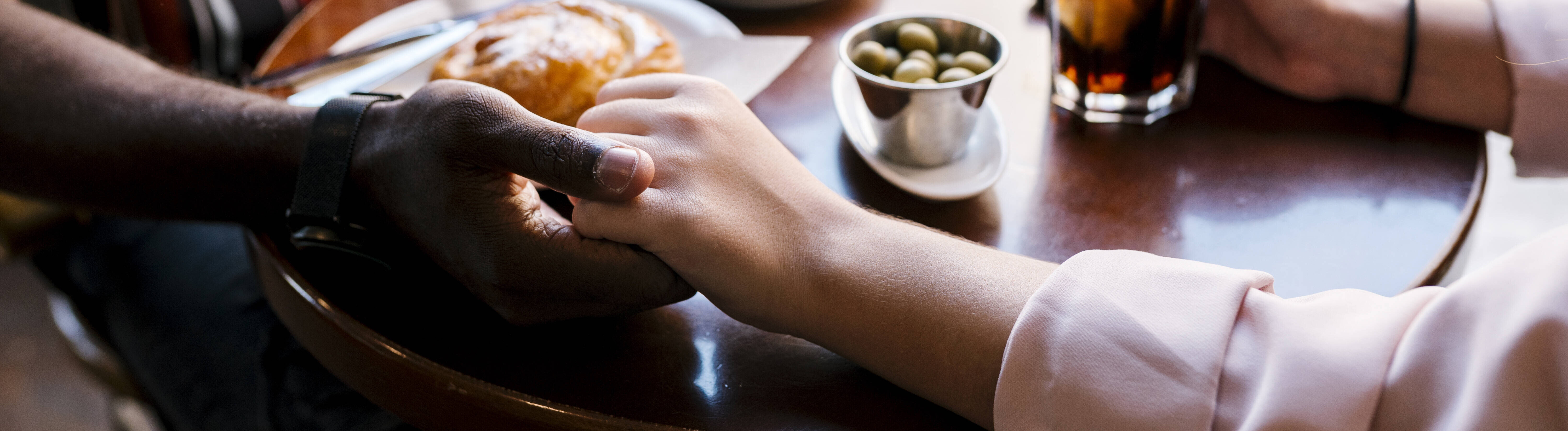 Nahaufnahme der Arme und Hände eines Pärchens, die im Café auf dem Tisch Händchen halten
