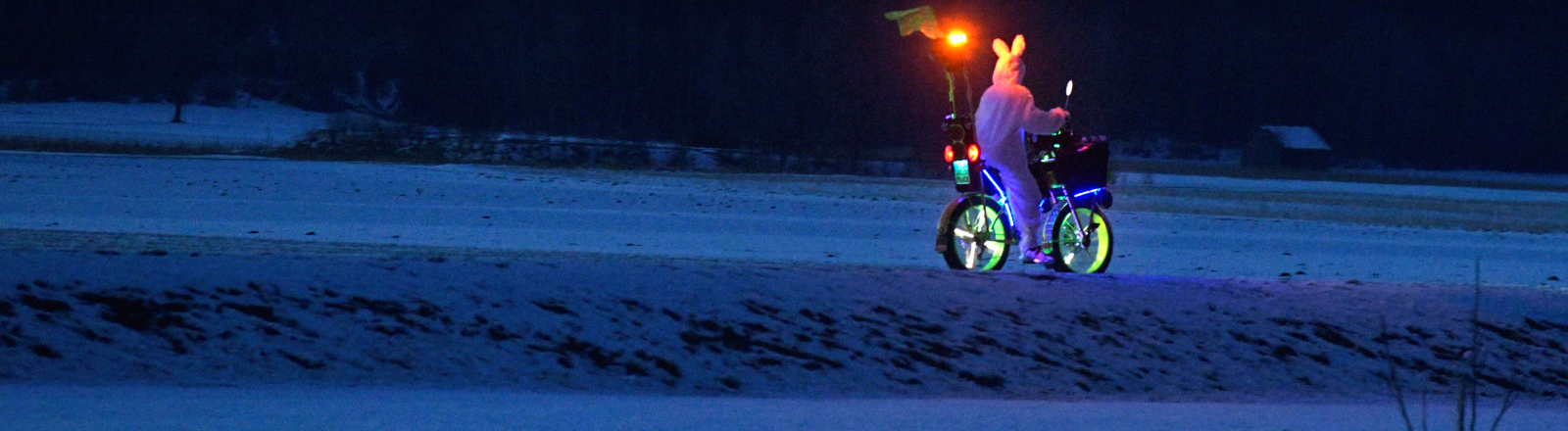 Bad Wörishofen im Unterallgäu, ein lustig maskierter Radler im Hasen-Kostüm und skurril beleuchtetem E-Bike fährt in der Abenddämmerung durch die Landschaft.