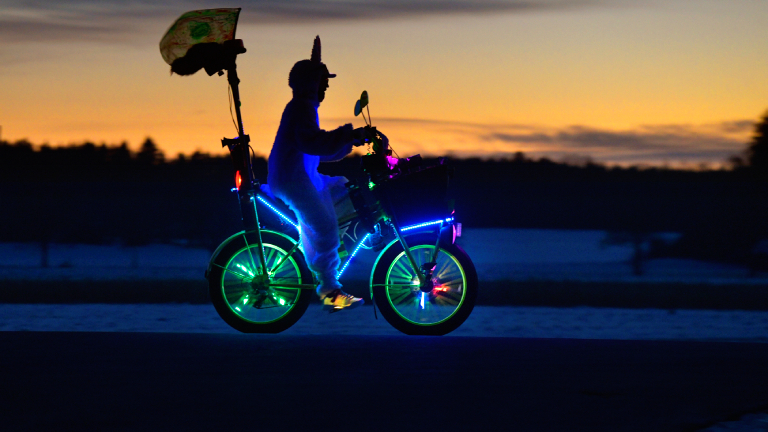 Bad Wörishofen im Unterallgäu, ein lustig maskierter Radler im Hasen-Kostüm und skurril beleuchtetem E-Bike fährt in der Abenddämmerung durch die Landschaft.