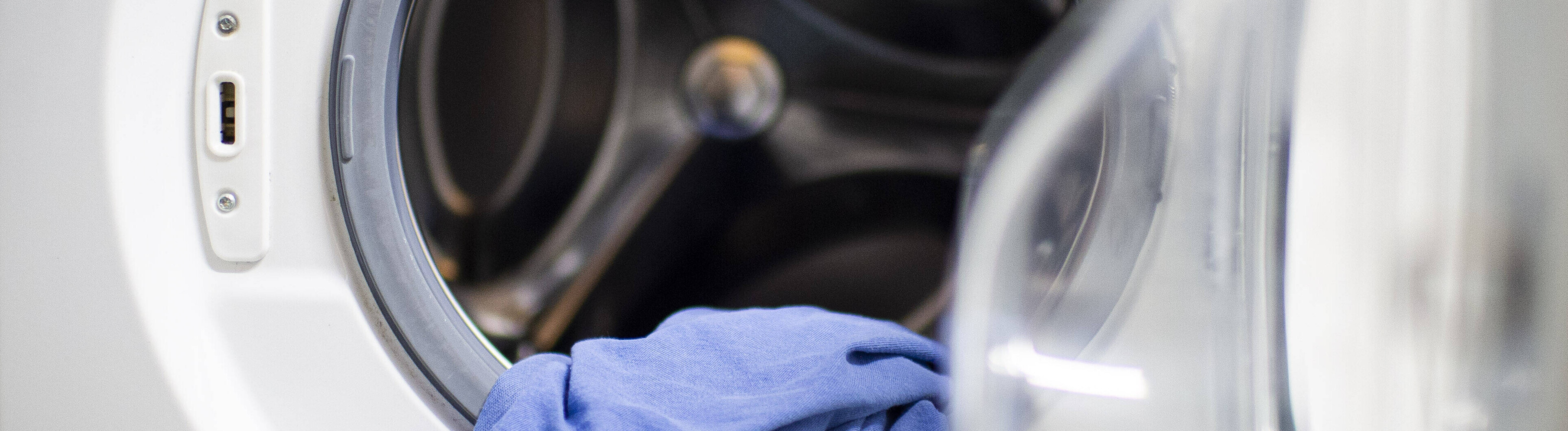 Aus einer geöffneten Waschmaschine hängt ein blaues Kleidungsstück.