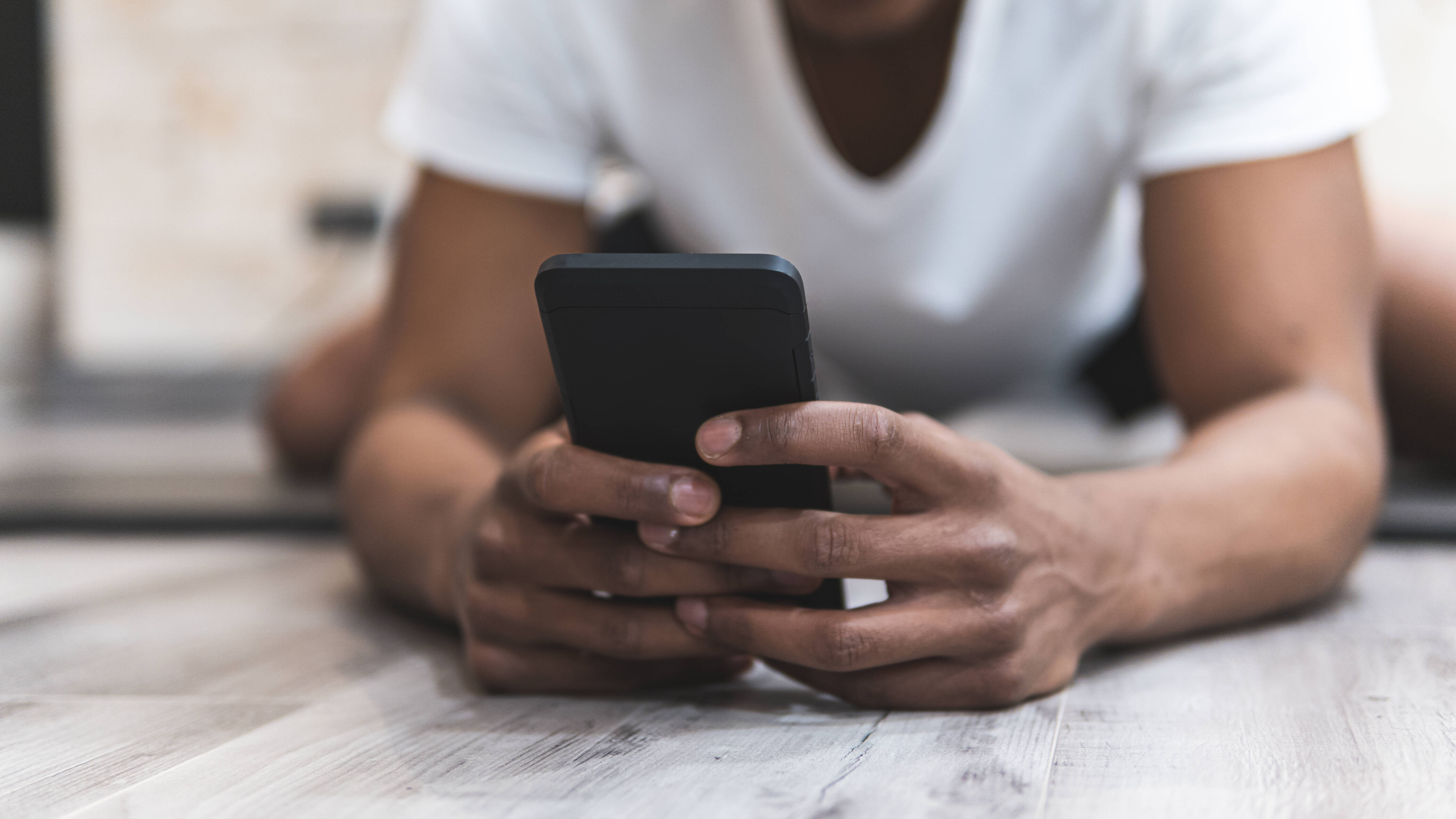 Foto eines jungen Mannes, der auf dem Fußboden liegend auf ein Smartphone guckt