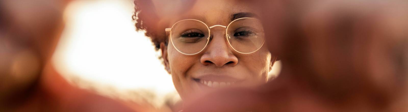 Eine Frau zeigt mit ihren Händen ein Herzsymbol. Sie lächelt.