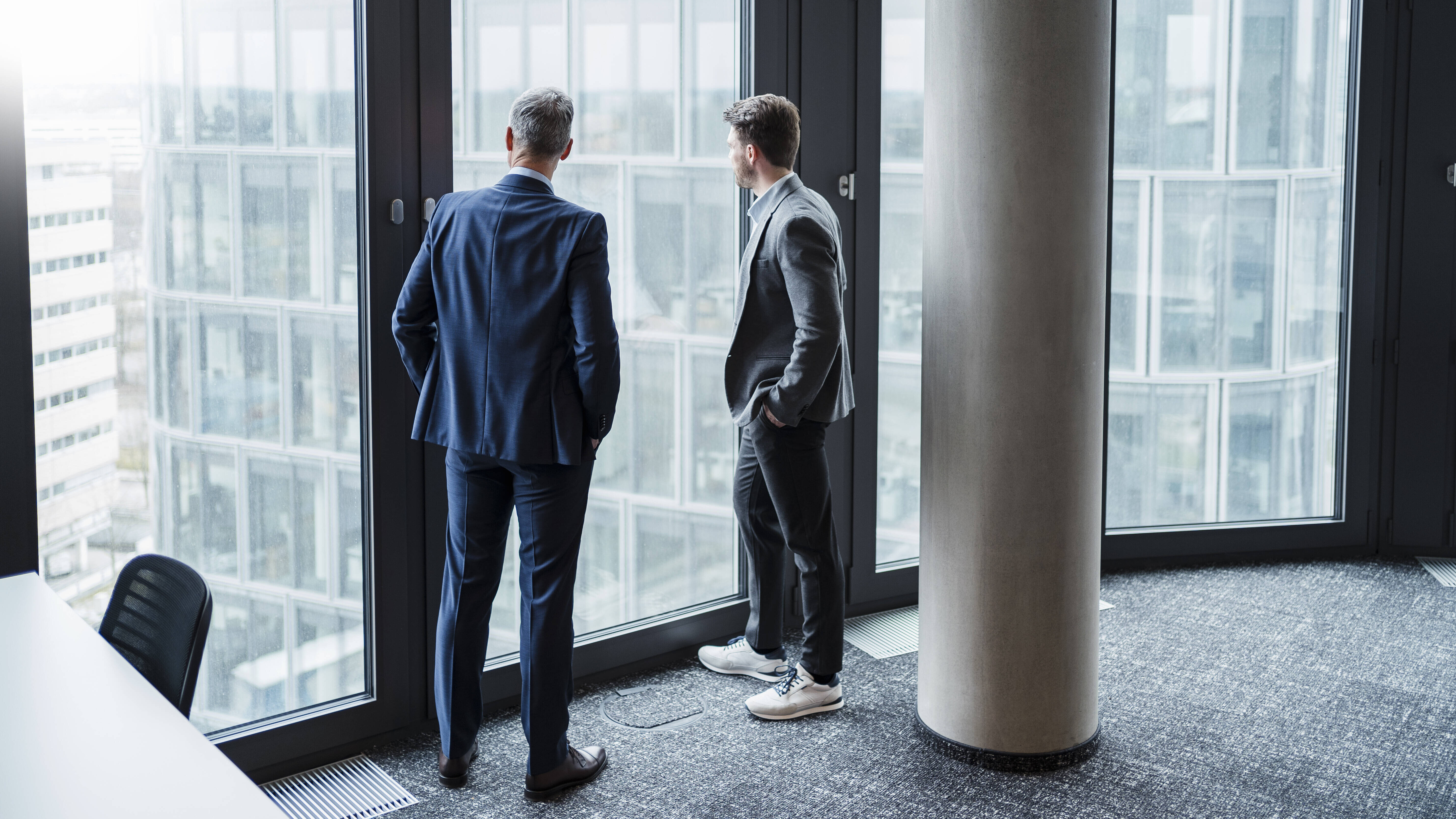 Geschäftsmann und sein Sohn/Nachfolger blicken durchs Fenster in Büro (Symbolfoto)