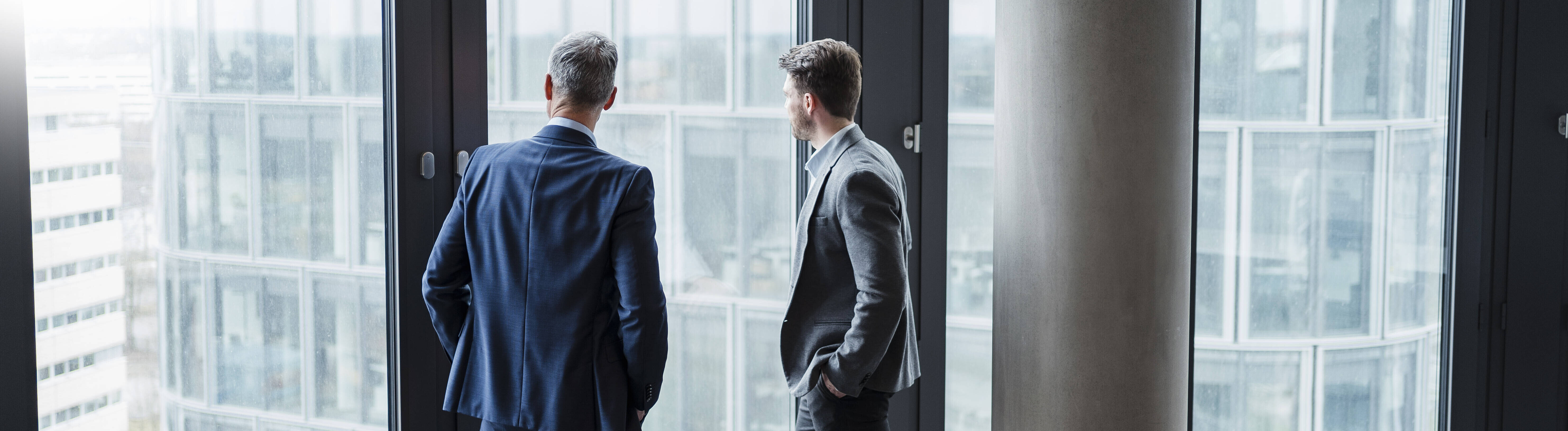 Geschäftsmann und sein Sohn/Nachfolger blicken durchs Fenster in Büro (Symbolfoto)