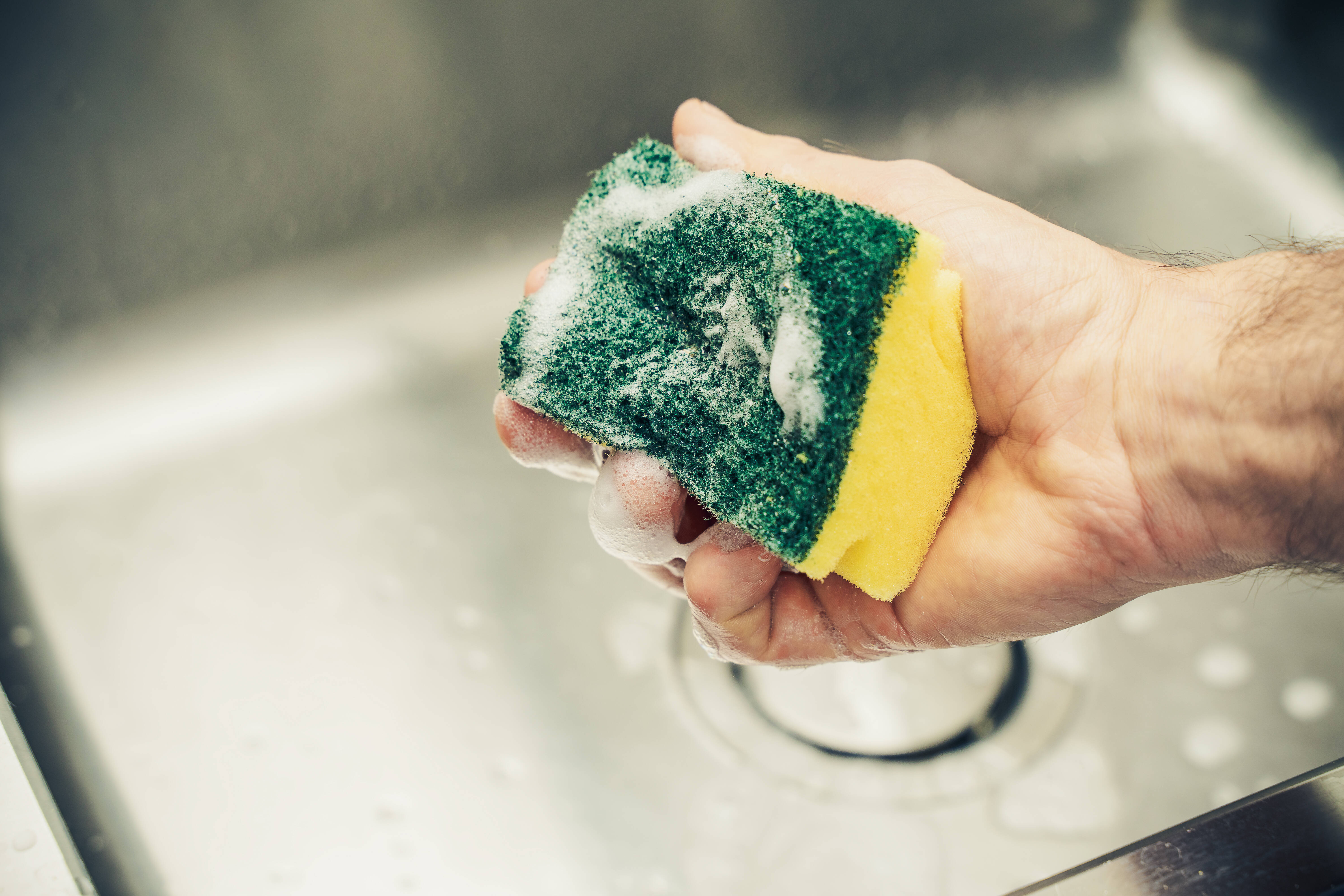 Ein Mann reinigt mit Schwamm und Spülmittel ein Waschbecken