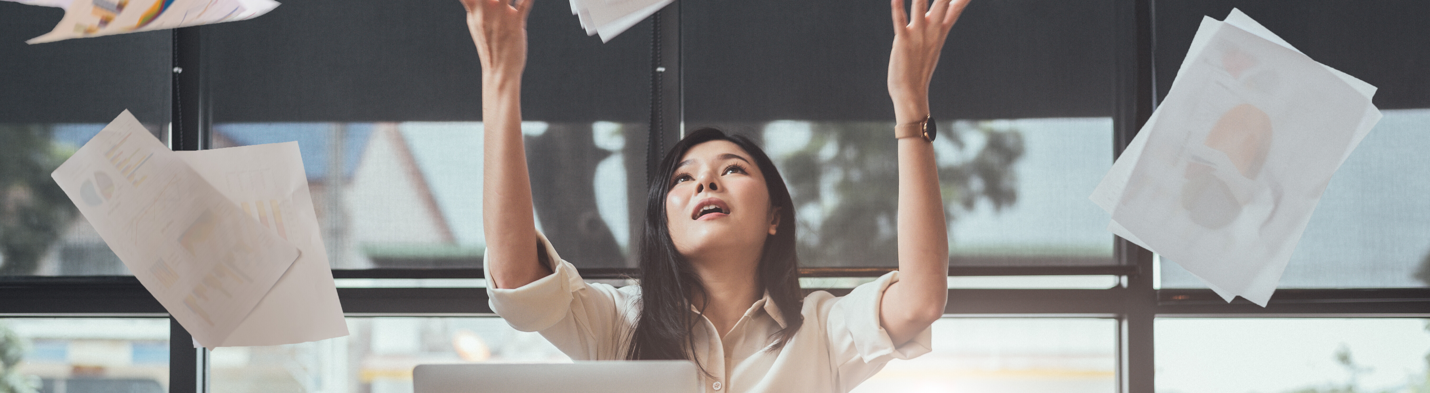 Eine Frau wirft an ihrem Arbeitsplatz Papierseiten in die Luft