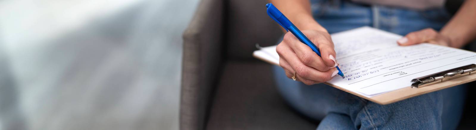 Im Wartezimmer sitzende Frau füllt ein Formular aus.