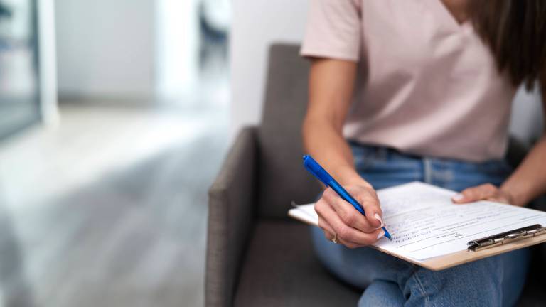 Im Wartezimmer sitzende Frau füllt ein Formular aus.