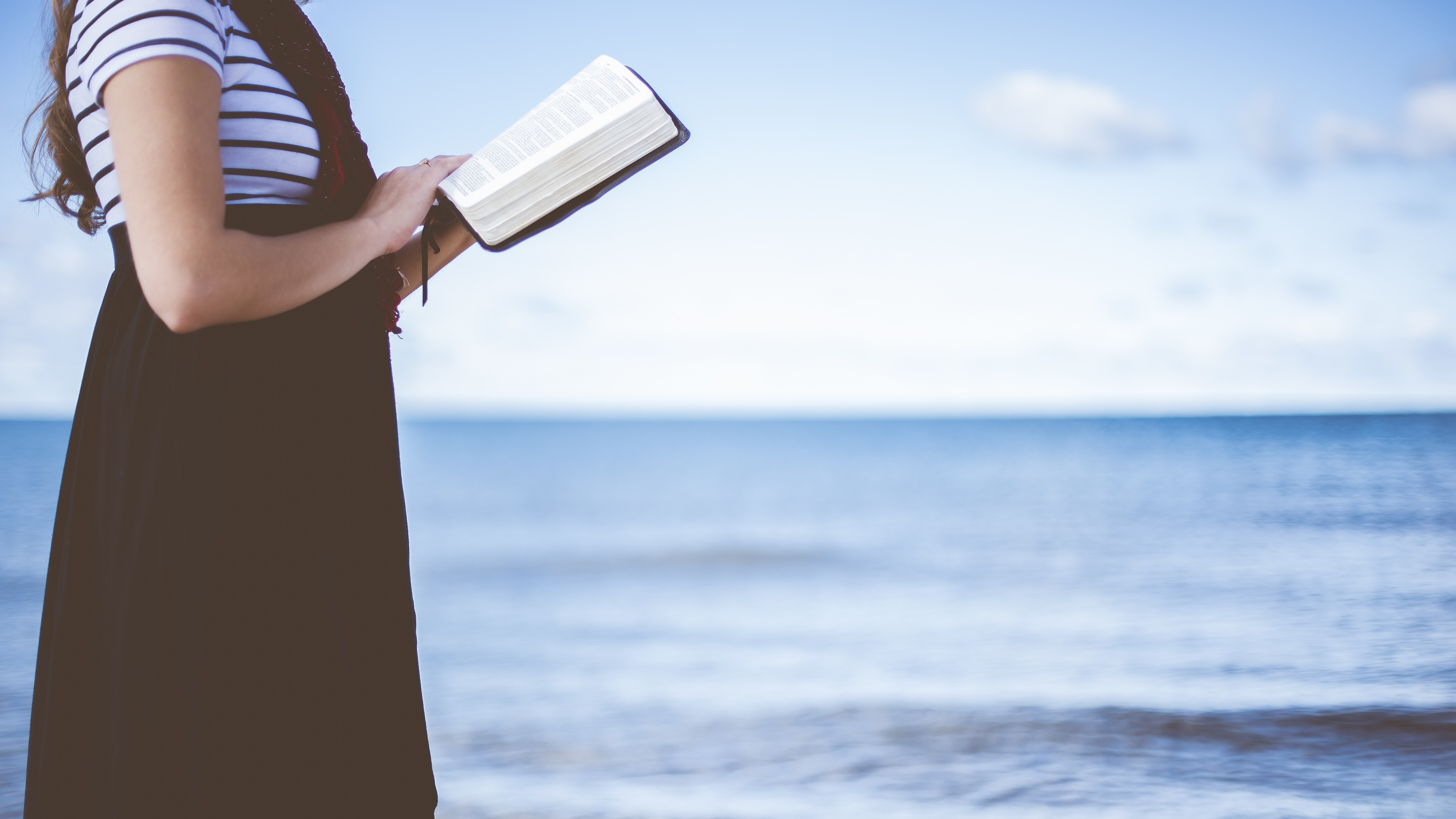 Eine Frau liest gehend ein Buch am Strand.