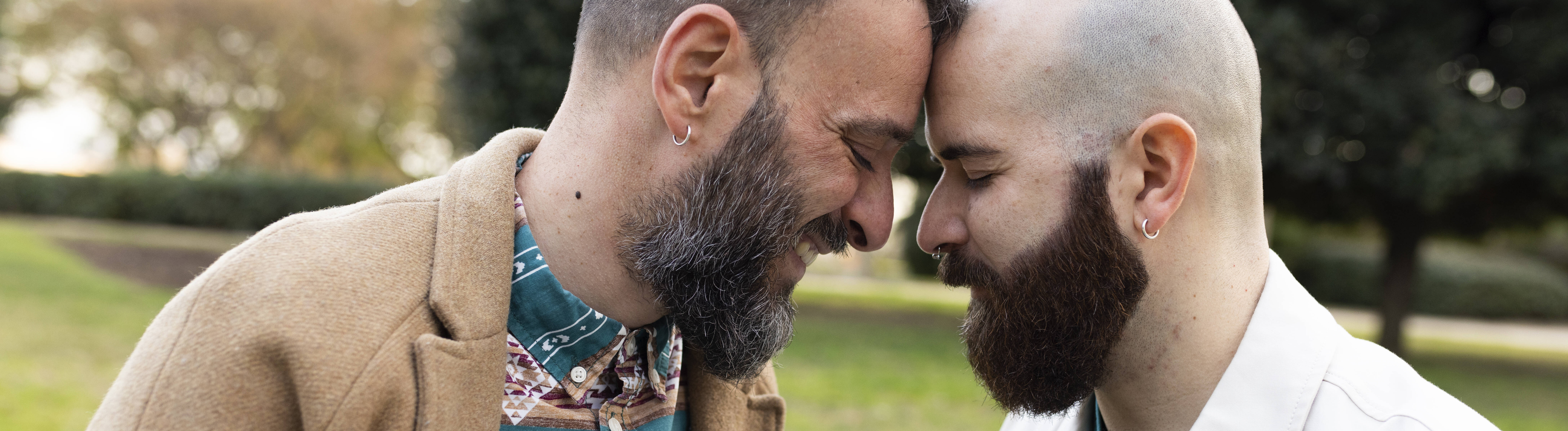Zwei Männer lehnen ihre Köpfe liebevoll gegeneinander. Sie wirken vertraut.
