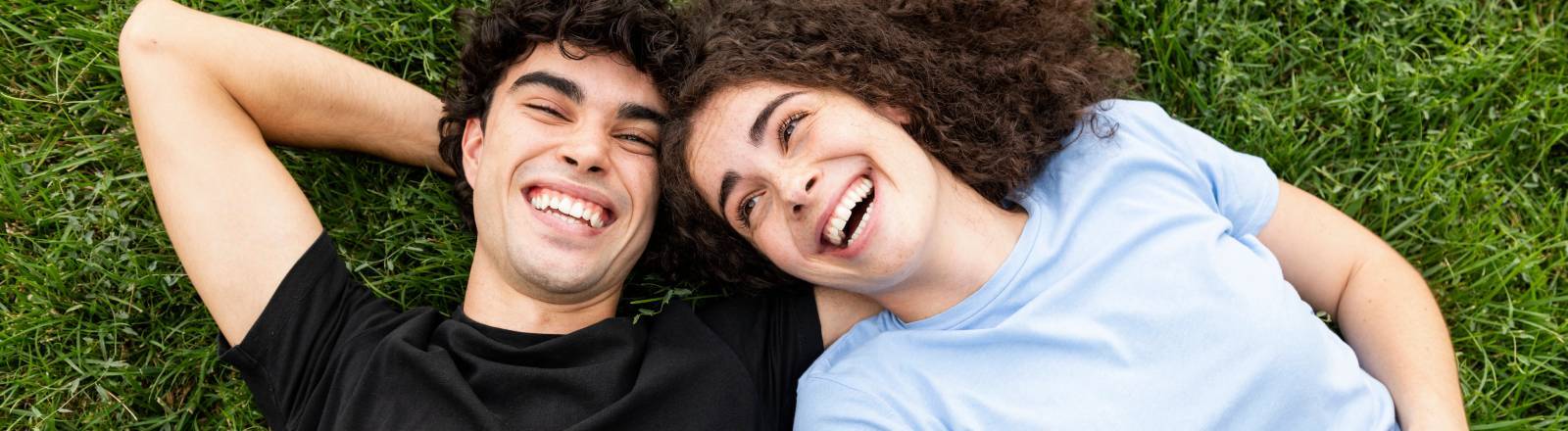 Ein junges Paar liegt im Gras und lacht