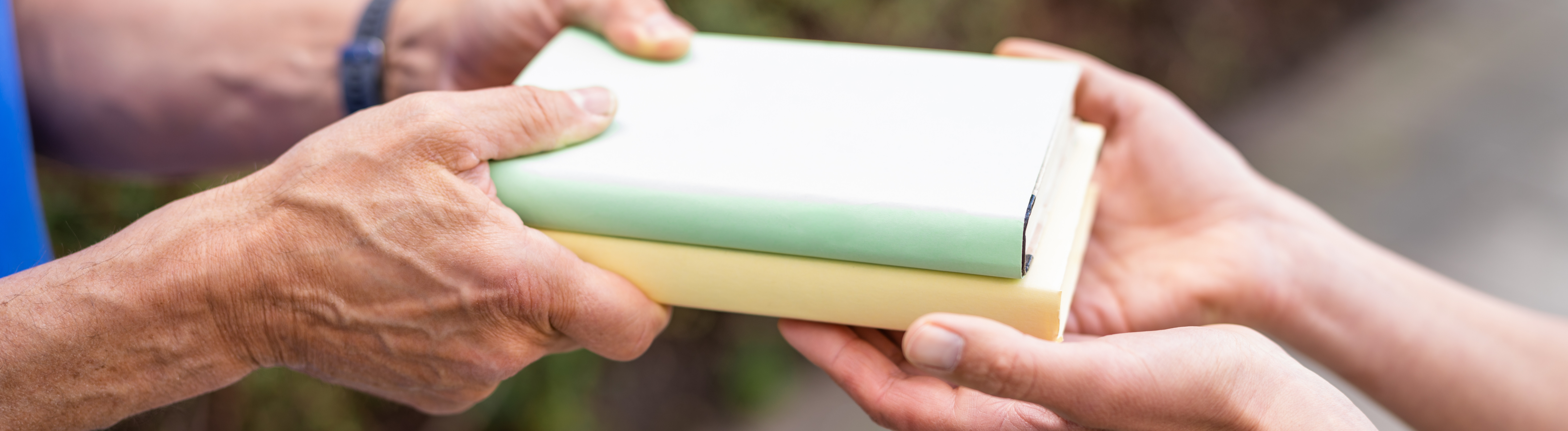 Hände einer männlichen Person übergeben zwei Bücher in die Hände einer weiblichen Person.