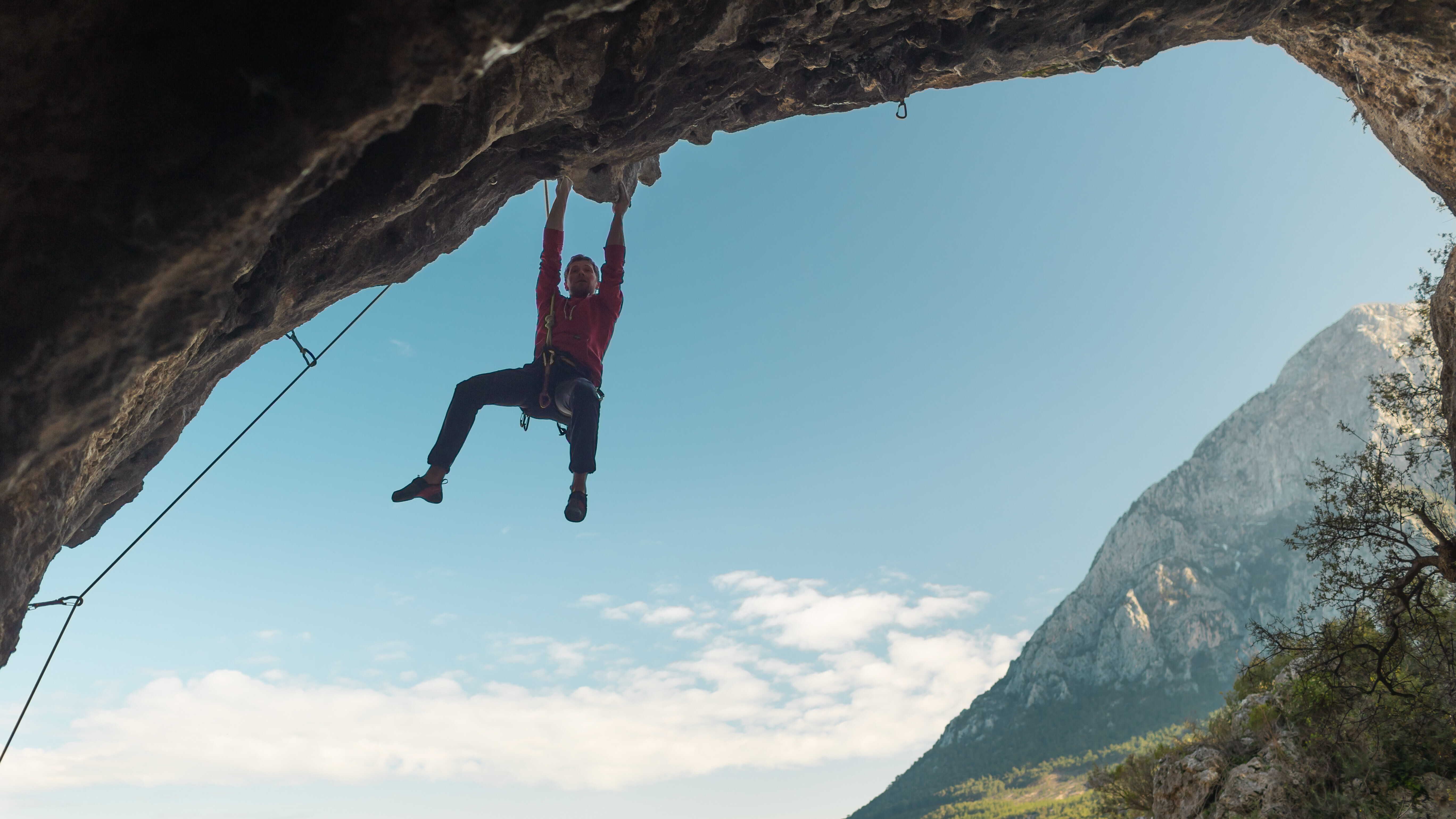 Ein Kletterer hängt mit beiden Händen an einer bogenförmigen Felswand