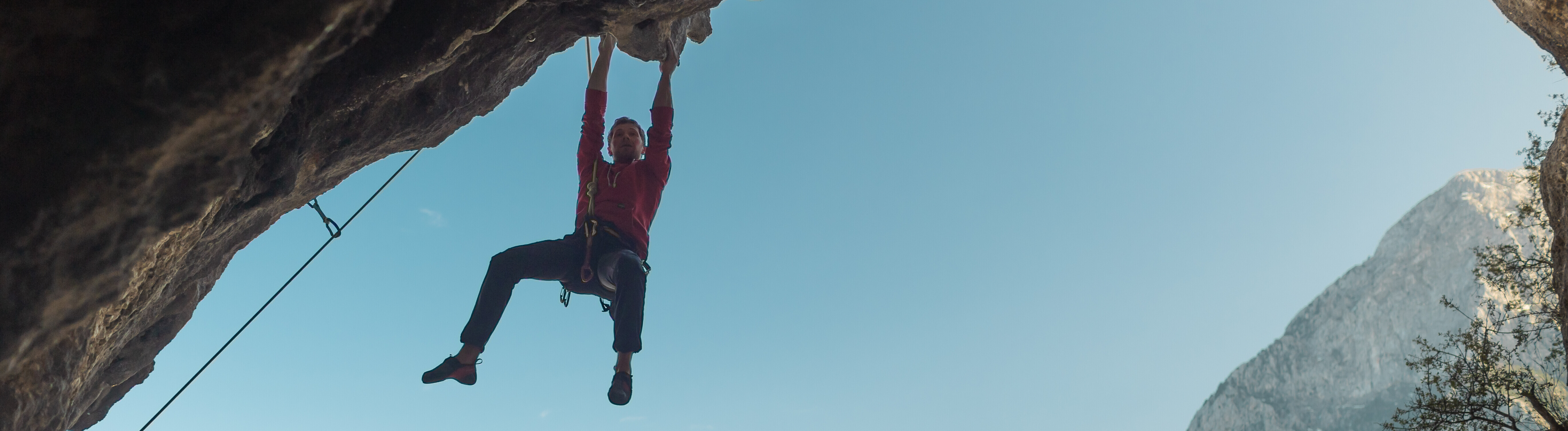Ein Kletterer hängt mit beiden Händen an einer bogenförmigen Felswand