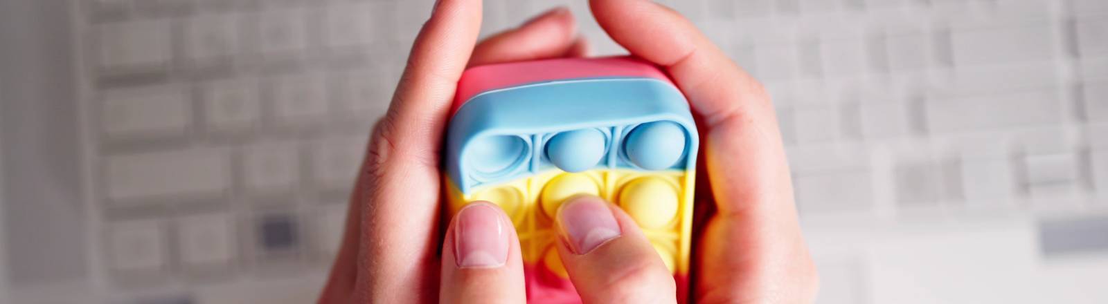 Finger drücken auf buntem Anti-Stress-Spielzeug rum; darunter liegt eine Tastatur