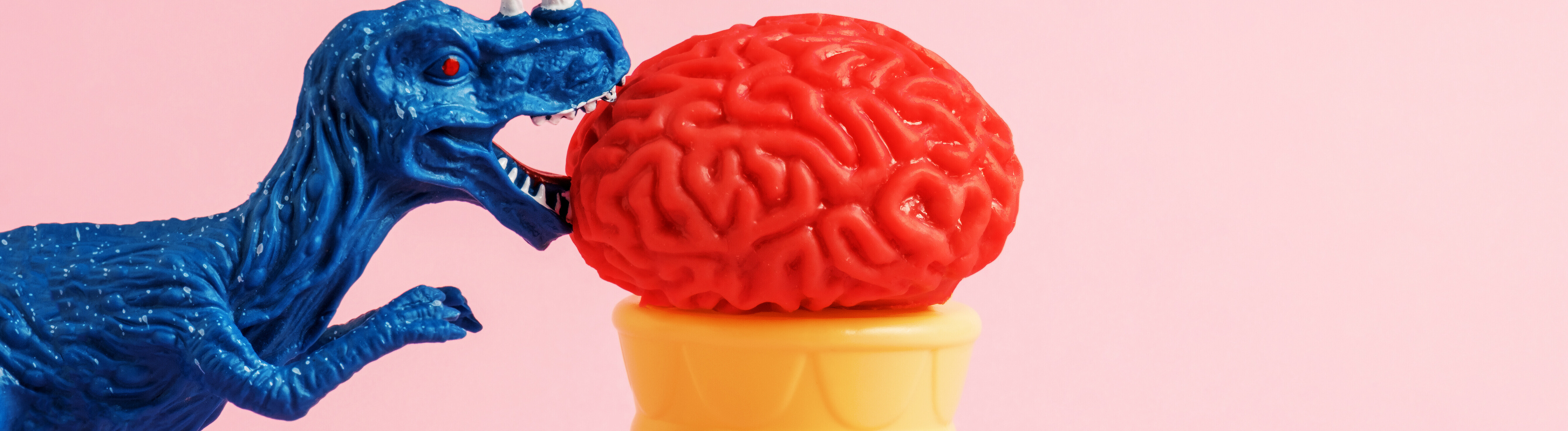 Symbolbild: Ein blauer Dinosaurier beißt in eine rote Eiskugel in Form eines Gehirns