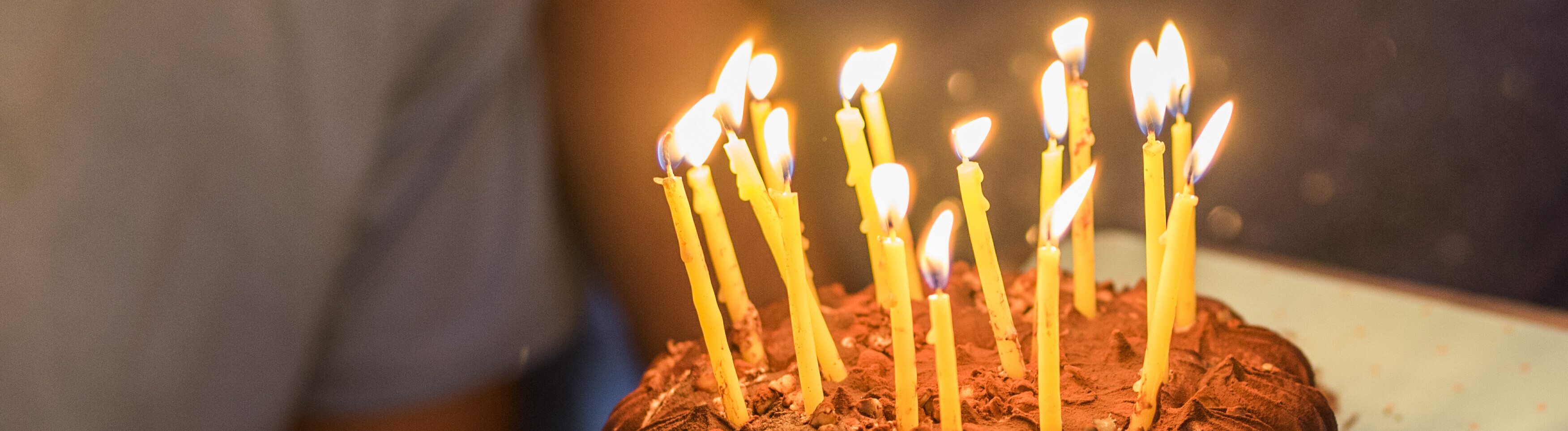 Ein junger Mensch lächelt, vor ihm ein Geburtstagskuchen mit brennenden Kerzen