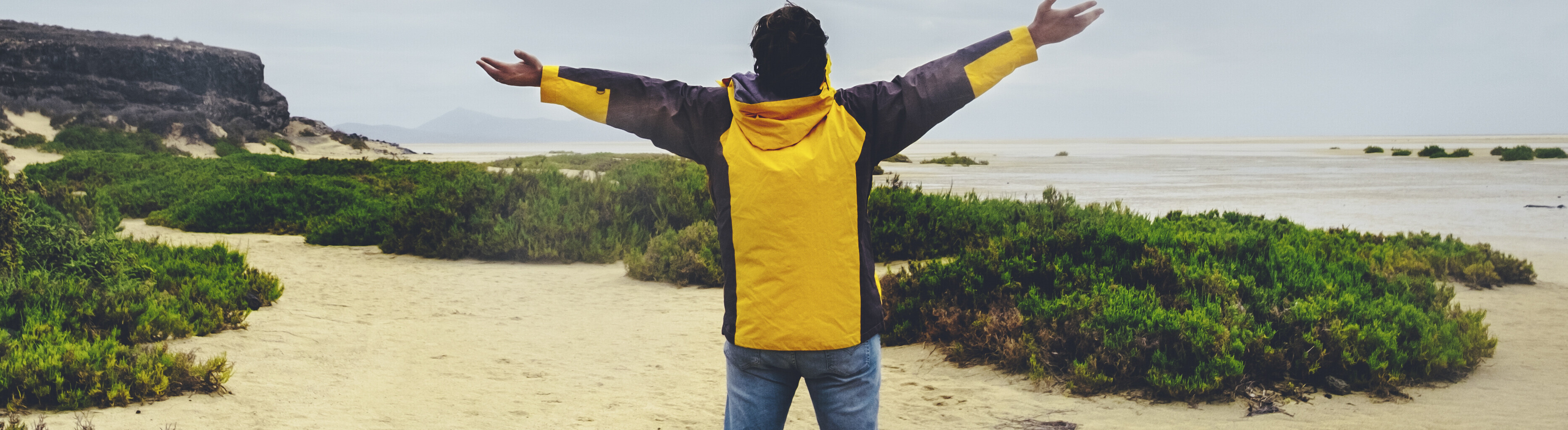 Ein Mann streckt an einem Strand anscheinend jubelnd die Arme aus.