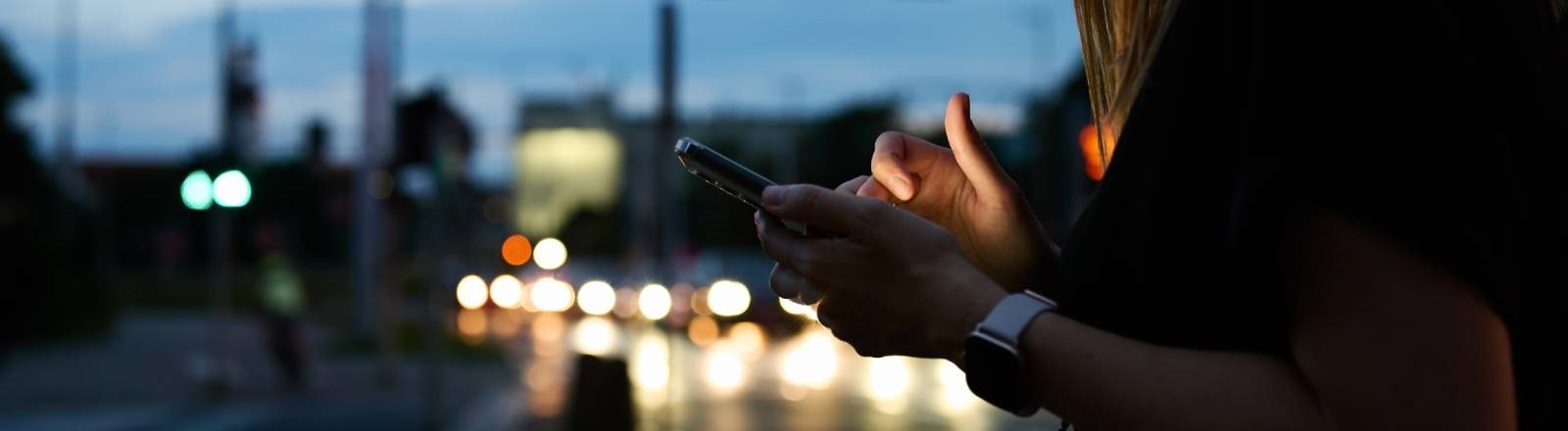 Eine Frau gibt etwas auf einem Smartphone ein, während sie draußen unterwegs ist
