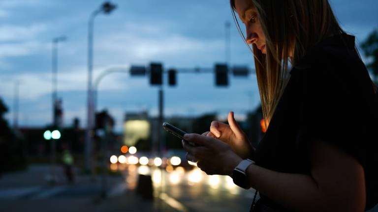 Eine Frau gibt etwas auf einem Smartphone ein, während sie draußen unterwegs ist