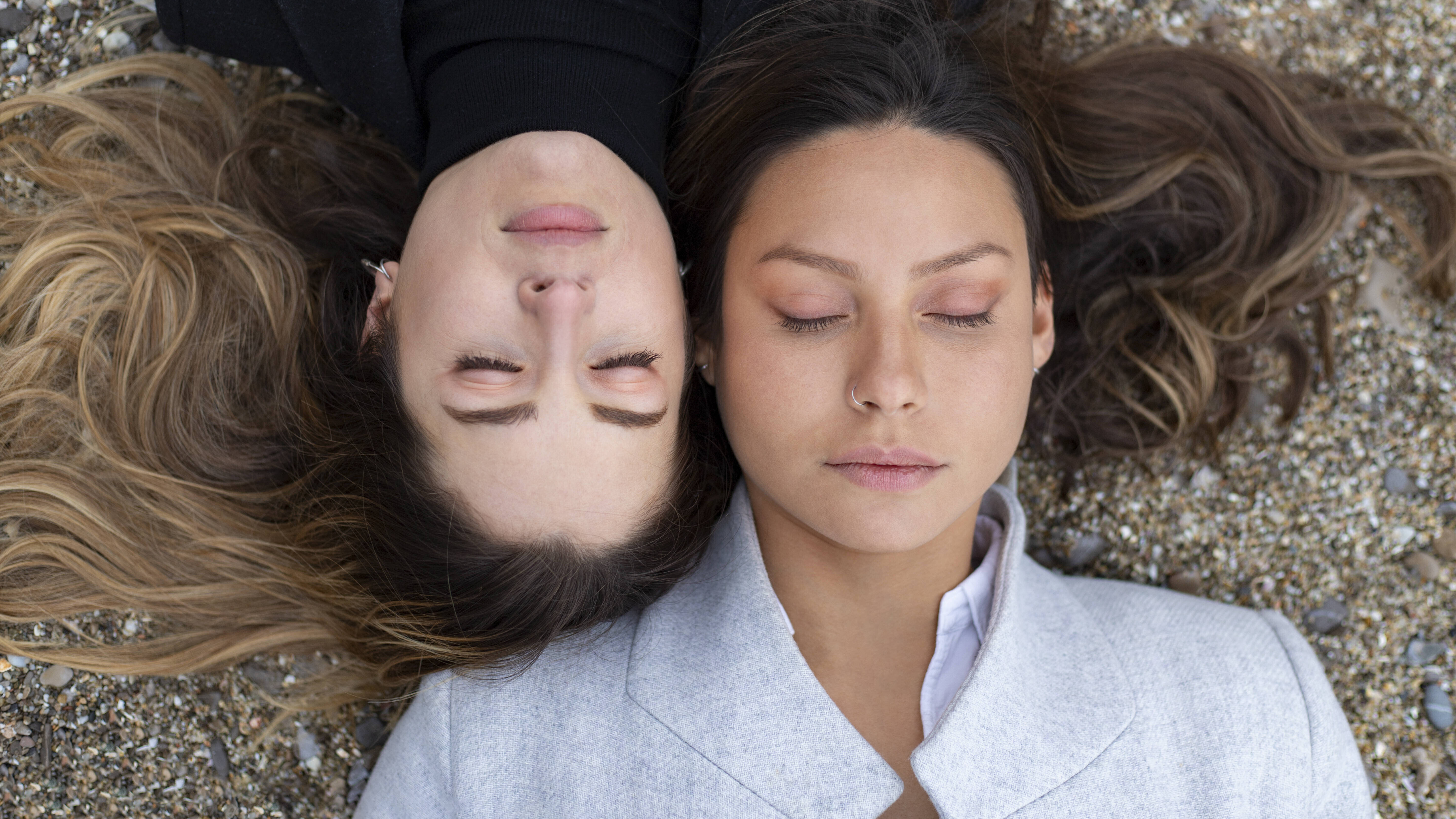 Zwei Frauen liegen versetzt zueinander auf dem Rücken und haben ihre Augen geschlossen. Ihre Köpfe liegen nebeneinander.