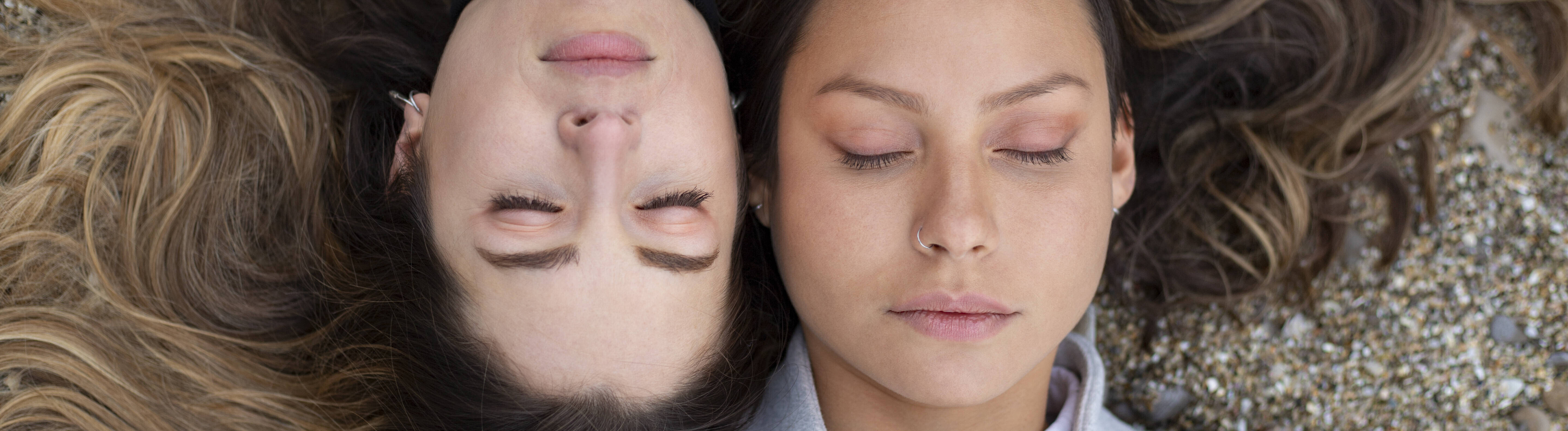 Zwei Frauen liegen versetzt zueinander auf dem Rücken und haben ihre Augen geschlossen. Ihre Köpfe liegen nebeneinander.