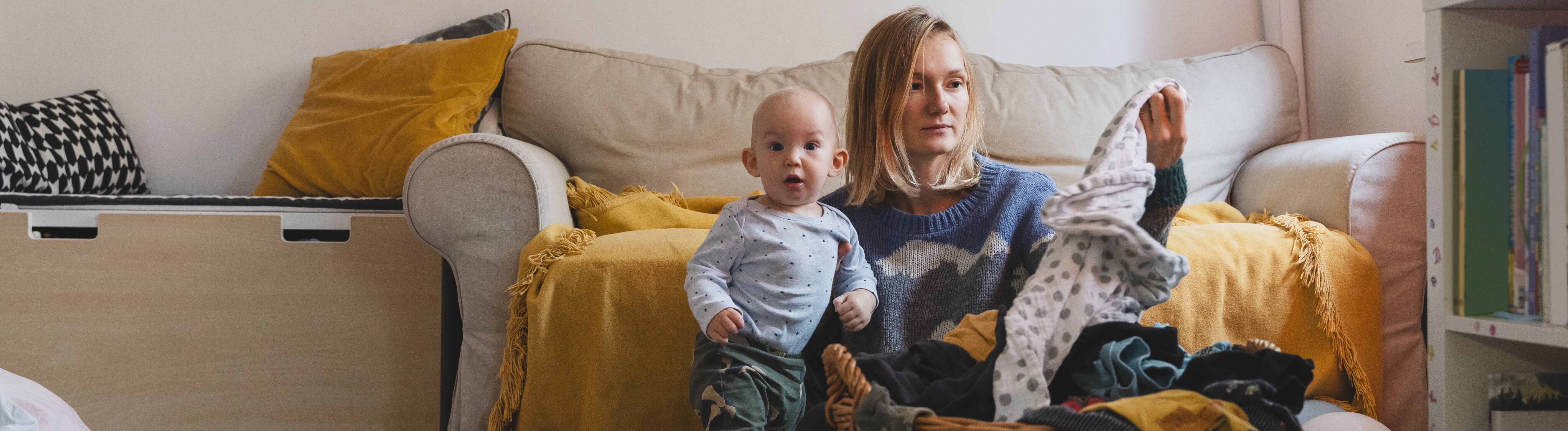 Foto einer jungen Frau, die mit ihrem Kind im Wohnzimmer auf em Boden sitzt und gewaschene Wäsche faltet