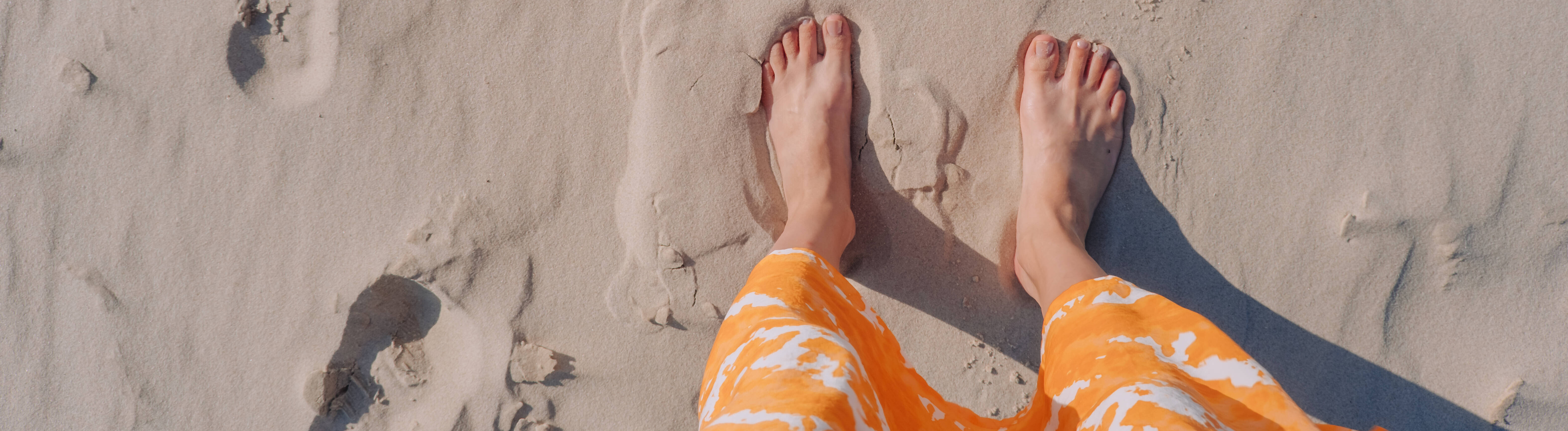 Eine Frau in einem orangefarbenen Rock steht barfuß an einem Strand