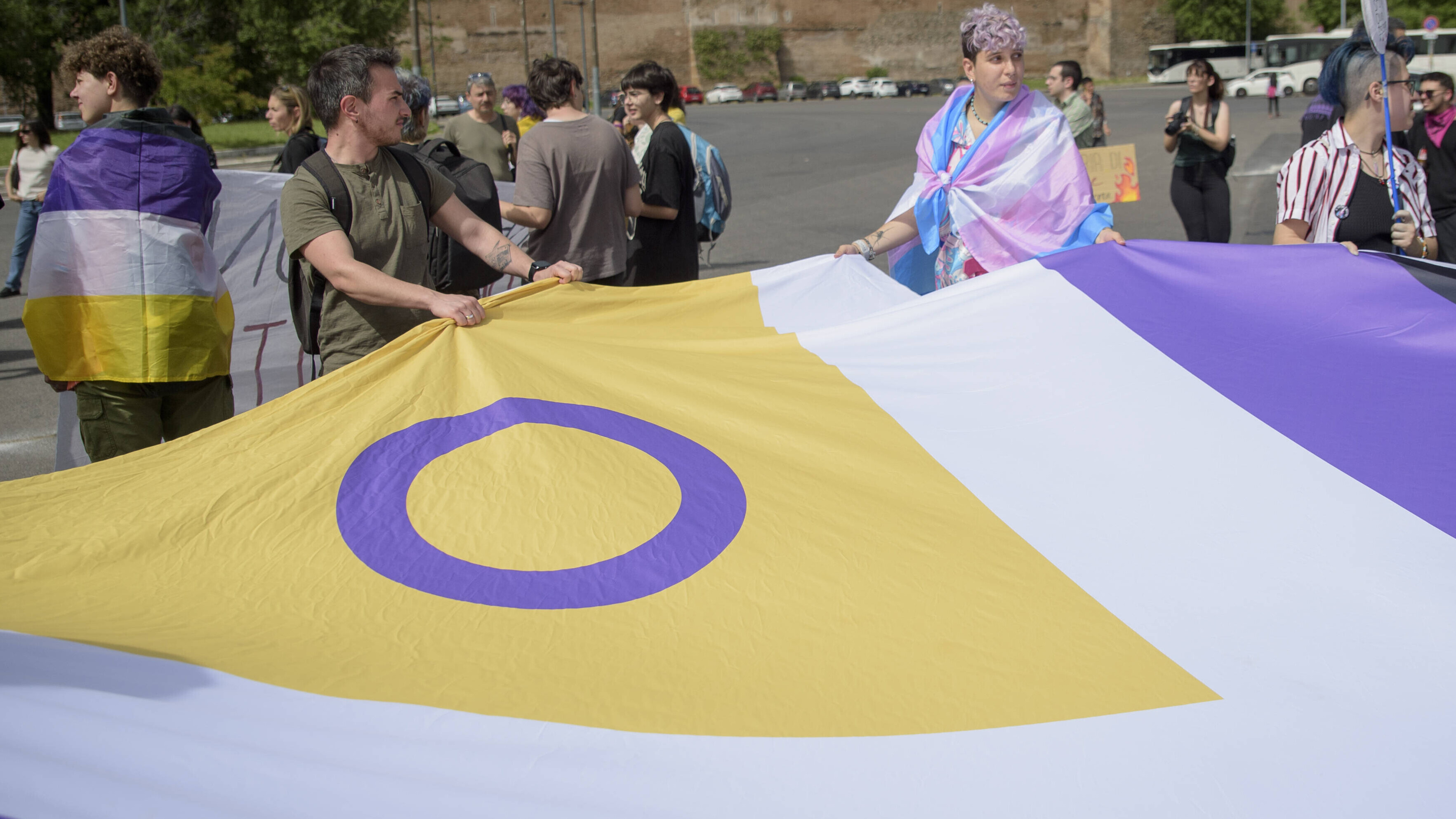 Auf einer Demonstration in Rom tragen Teilnehmende eine große Flagge mit dem Symbol der Inter*-Bewegung, einem lila Kreis auf gelbem Hintergrund. Die Flagge ist für Menschen, die sich als intergeschlechtlich identifizieren.