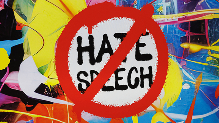 Foto eines bunten Plakats im Graffiti-Stil auf dem in roter Faden ein Stoppzeichen gesprüht ist, auf dem "Hate Speech" steht
