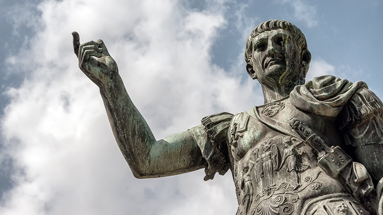 Untersichtige Fotografie einer Bronzestatue des römischen Kaisers Caesar Nervae Trajan vor weiß bewölktem blauen Himmel