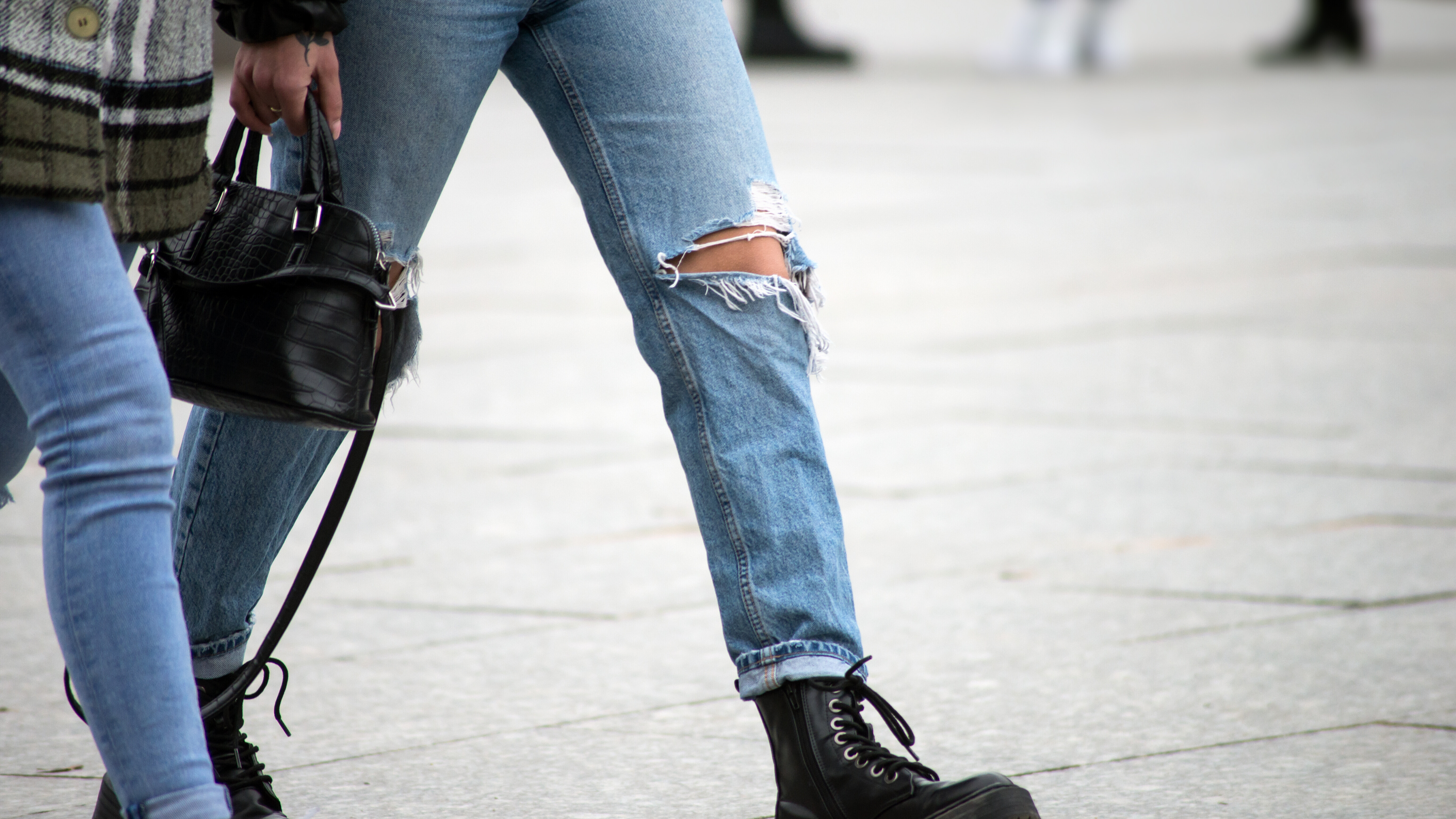 Zwei Frauen gehen mit einer Handtasche und zerrissenen Jeans über einen Platz
