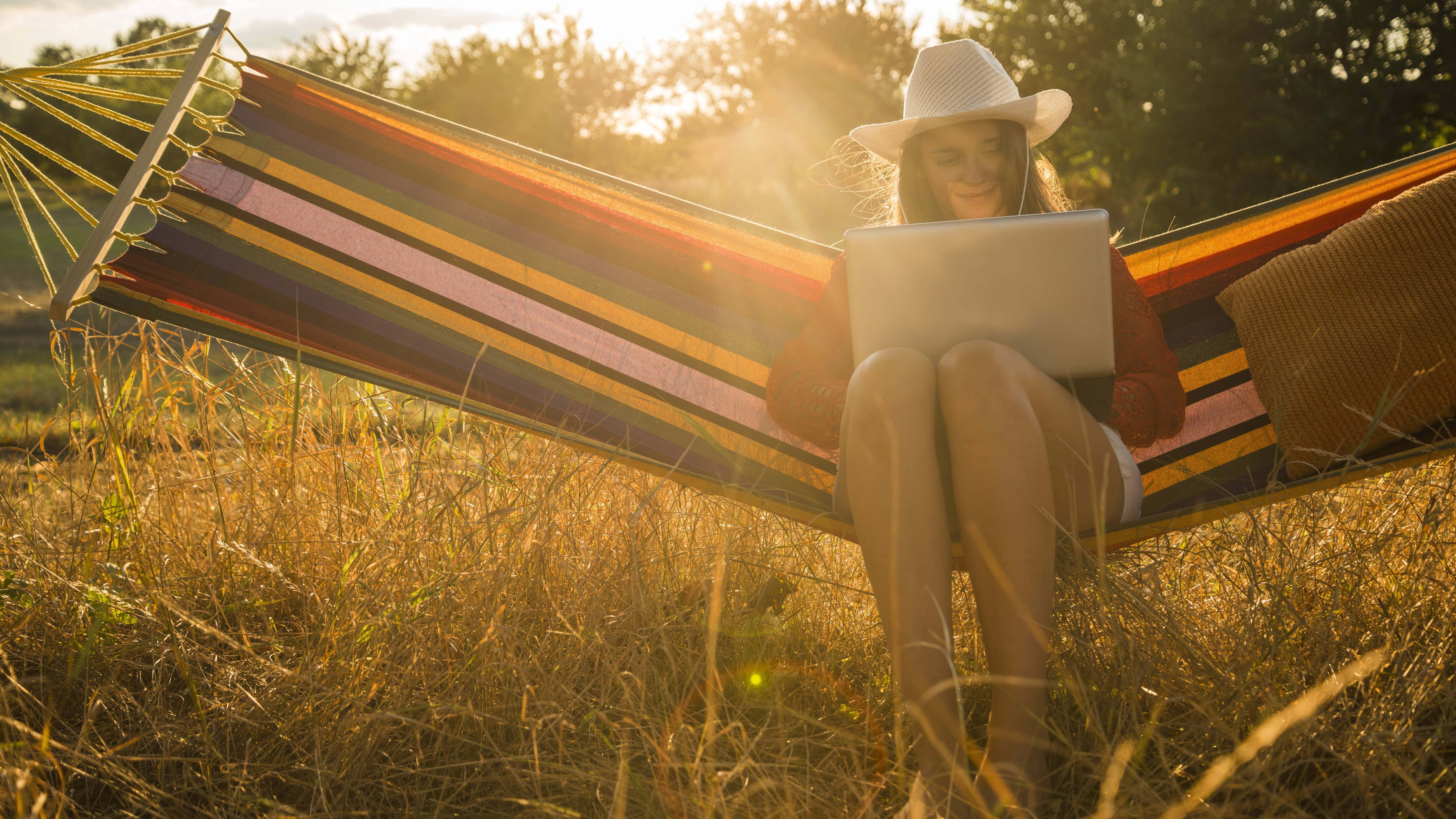 Eine Frau sitzt mit einem Laptop in einer Hängematte
