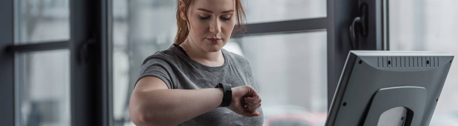 Eine Frau auf einem Laufband schaut auf ihren Fitnesstracker